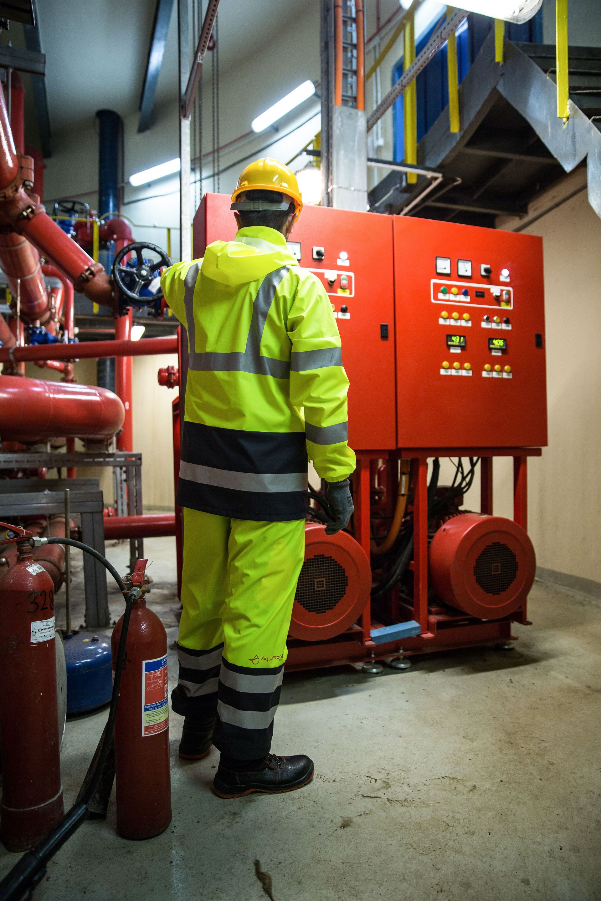 Engineer in high-visibility uniform operates control panel in industrial setting.