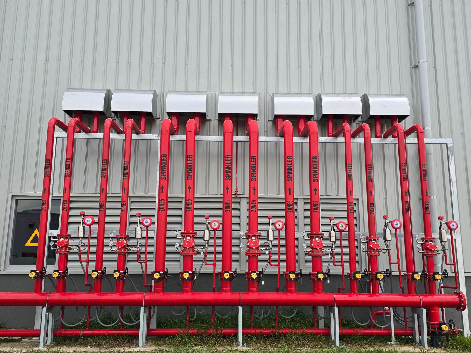 Red industrial fire sprinkler pipes aligned on a factory exterior wall.