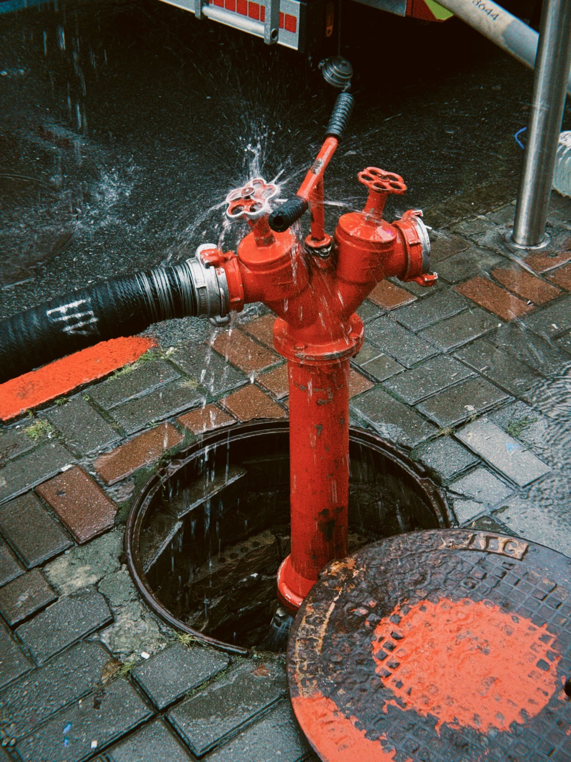 Red fire hydrant connected to a hose with water spraying.